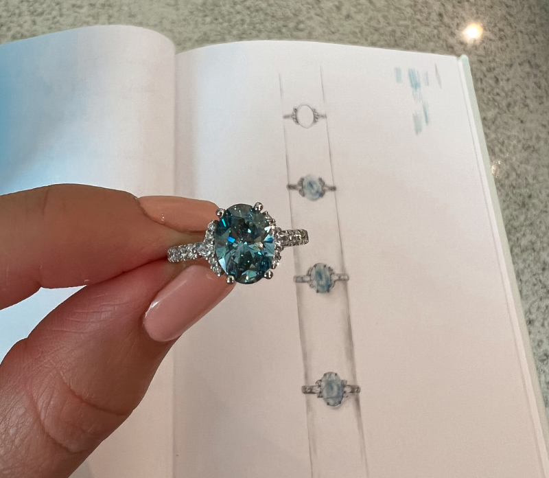 Designer Diamonds: Designe mit uns deinen Traumverlobungsring oder suche dir einen aus unserer Auswahl aus! Die besten Diamantverlobungsringe in München. Auf dem Bild ist ein silberner Verlobungsring mit einem Edelstein aus Aquamarine und kleinen Diamanten zu sehen.